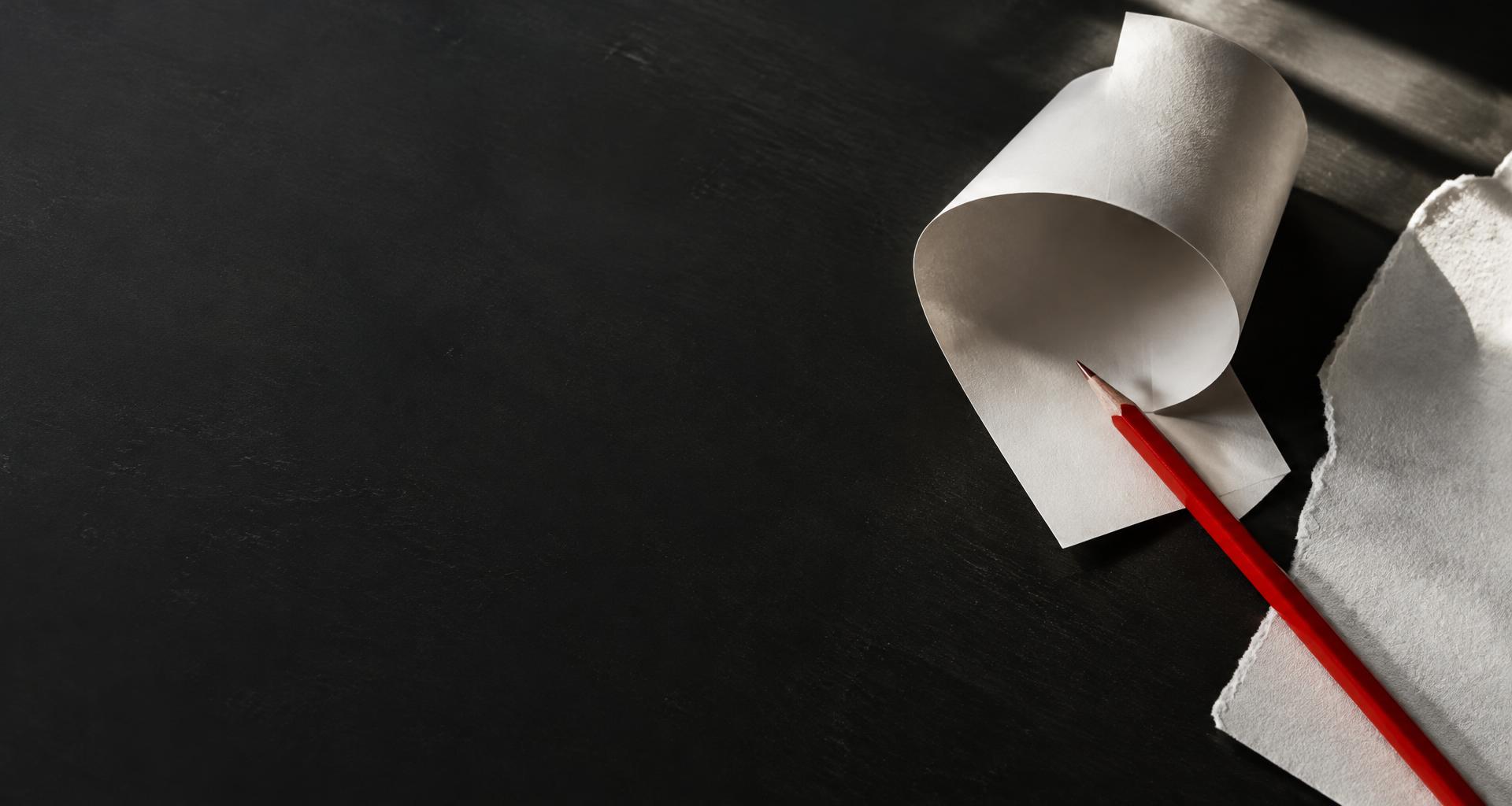 An unwritten sheet of paper and a red pencil on a dark desk